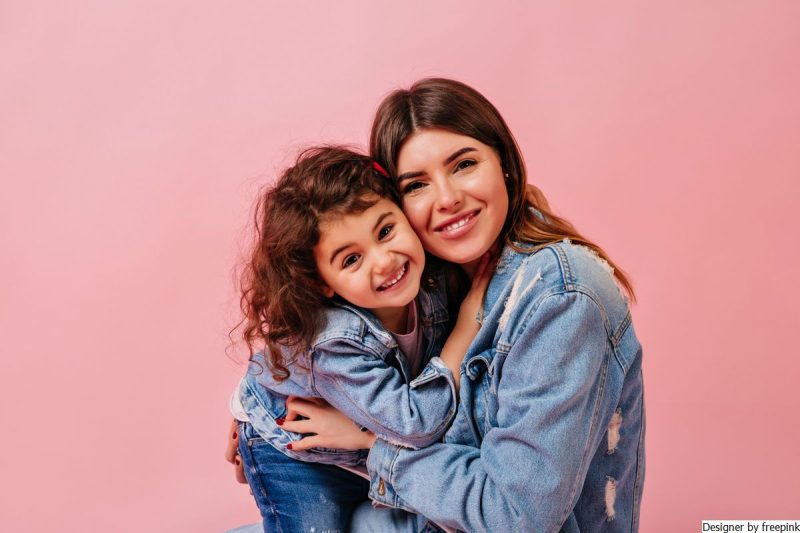 mãe sorrindo com filha no colo. Representando a importância das regras para o equilíbrio emocional das crianças.