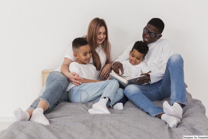 pai e mãe vestidos de blusa branca e calça jeans estão lendo com os dois fihos representando inteligência emocional.