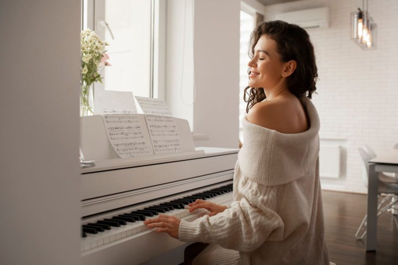 mulher, com blusa de manga comprida branca tocando um piano branco.