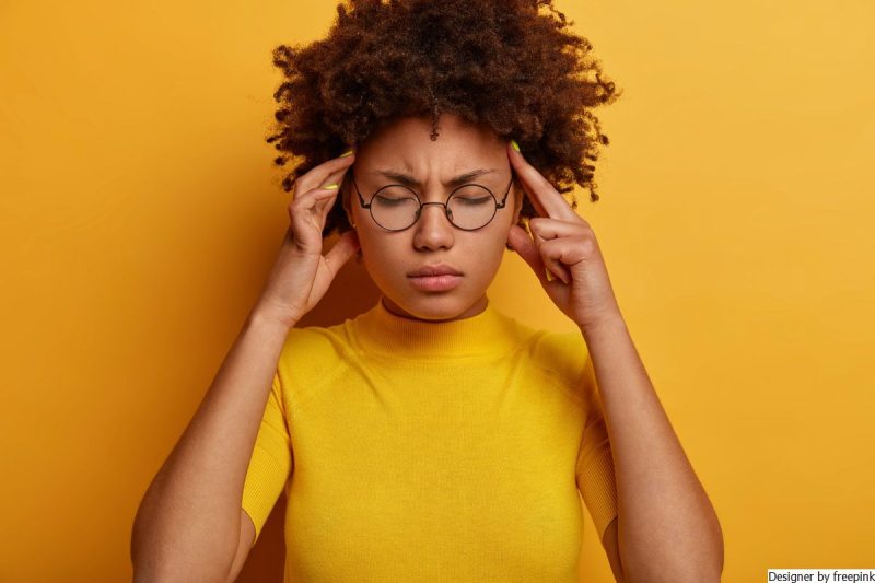 mulher jovem, está com as mãos nas têmporas e olhos fechados tentando se livrar da mente tagarela.