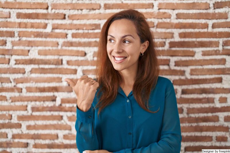 Mulher jovem, morena, usa blusa azul e está com o polegar para cima simbolizando assertividade.