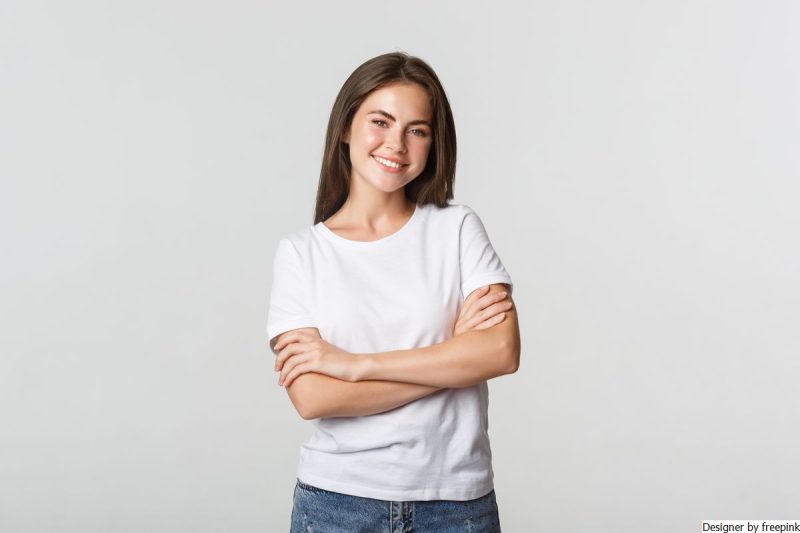 mulher jovem, cor branca, sorrindo. Usa blusa branca e calça jeans está simbolizando a preocupação excessiva em agradar.