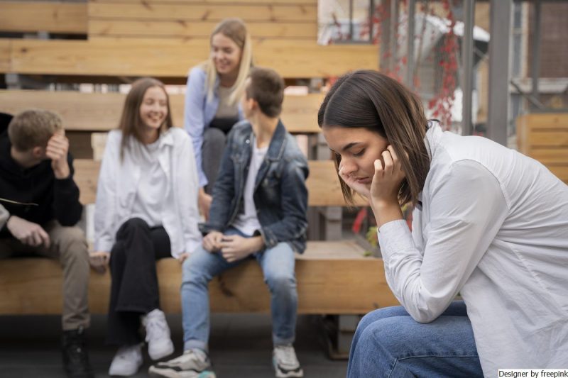 moça, isolada do grupo de amigos, usa blusa branca e calça jeans, simboliza a ansiedade social.