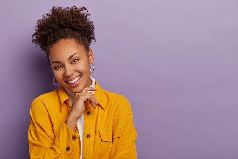 mulher negra, sorrindo, usa cabelo preso, jaqueta amarela com blusa branca de gola alta, mostra como lidar com situações difíceis.